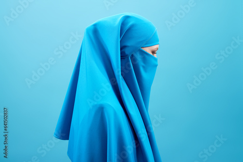 Profile portrait of mysterious woman in blue niqab against blue background   photo