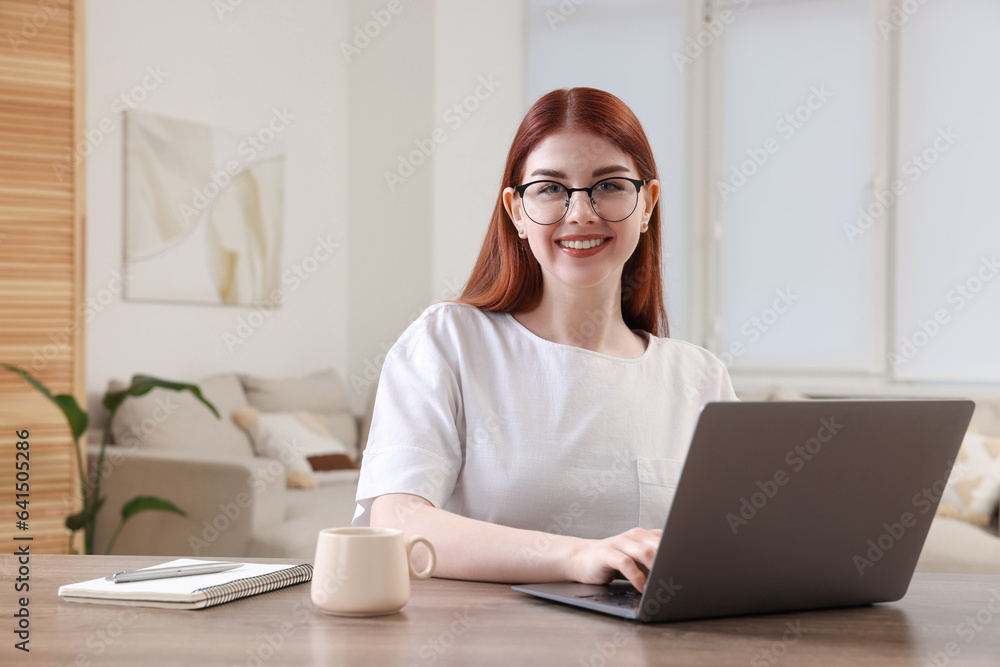 Happy woman using laptop at wooden table in room Happy woman using laptop at wooden table in room