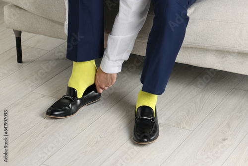 Man with yellow socks putting on stylish shoes indoors, closeup