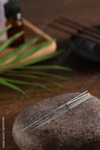 Acupuncture needles and spa stone on wooden table. Space for text