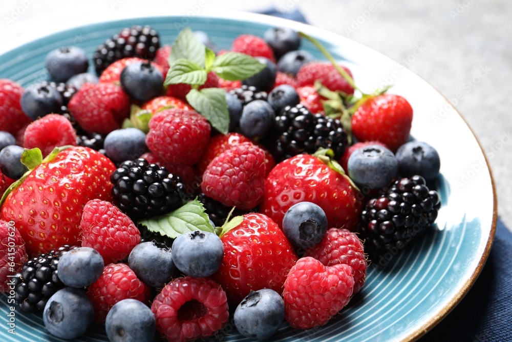 Many different fresh ripe berries in plate on grey table, closeup Many different fresh ripe berries in plate on grey table, closeup