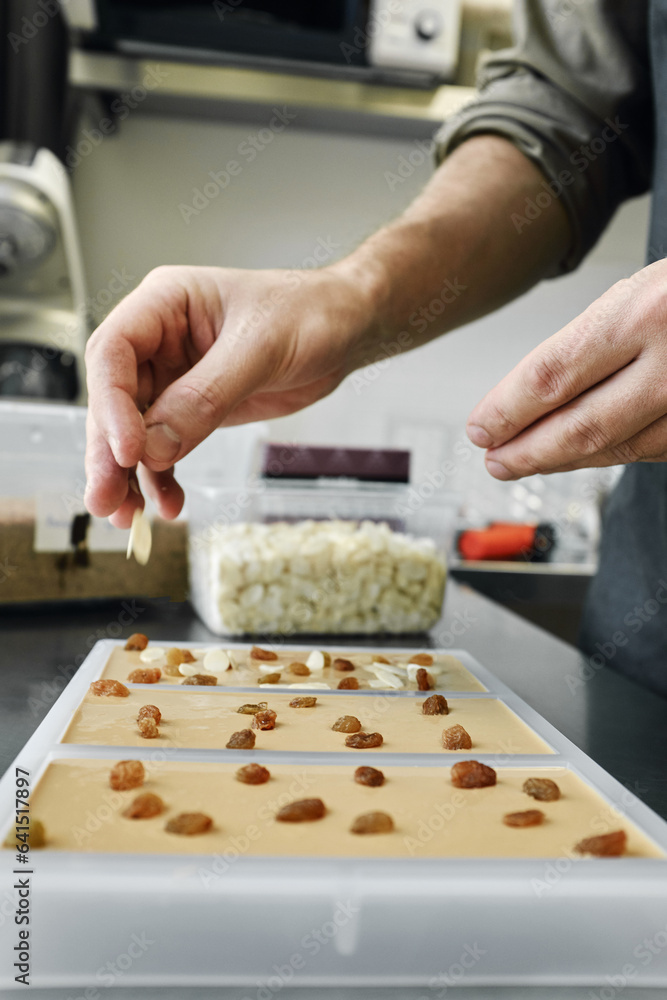 Close-up view of unrecognizable male cook making original white chocolate with raisins and sliced almonds in kitchen Close-up view of unrecognizable male cook making original white chocolate with raisins and sliced almonds in kitchen