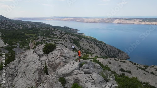aerial view of a couple standing atop cliffs, framed by the stunning landscape of Pag Island in the background. This enchanting scene unfolds during the vibrant Croatian summertime