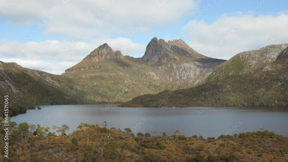 Fixed, wider shot of Cradle Mountain Tasmania, overlooking Dove Lake. Stunning mountain range in background of native shrubbery with blue sky and clouds. Famous tourist attraction. Fixed, wider shot of Cradle Mountain Tasmania, overlooking Dove Lake. Stunning mountain range in background of native shrubbery with blue sky and clouds. Famous tourist attraction.