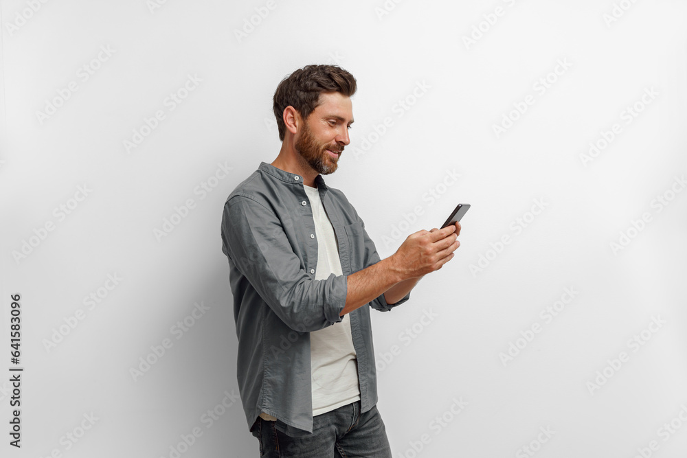 Smiling man looking to his mobile phone while standing on white background Smiling man looking to his mobile phone while standing on white background