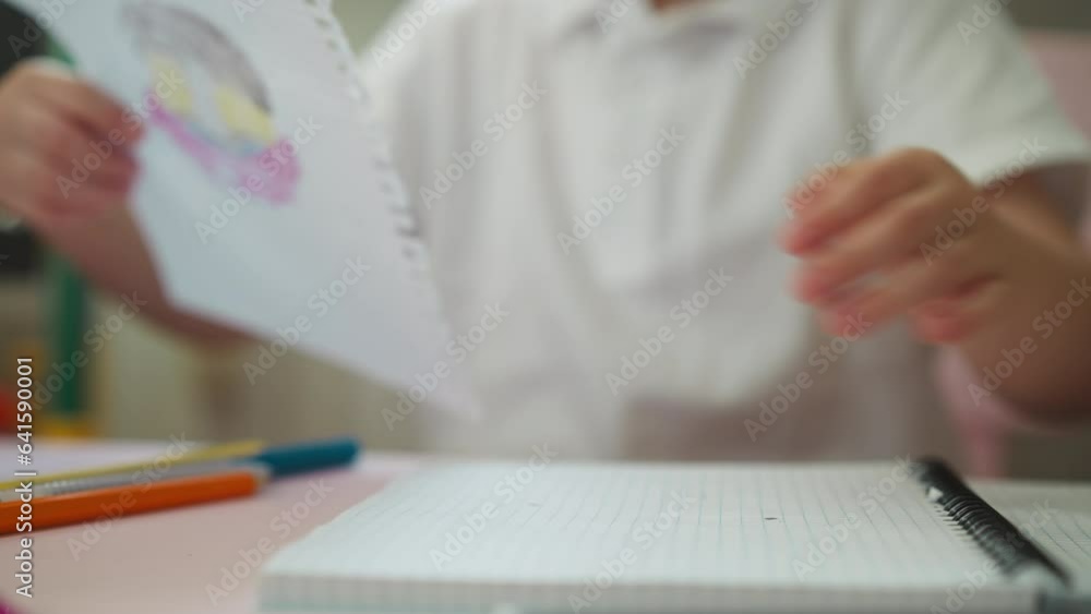 Little boy pulls to tear out notebook page with drawing at table closeup. Preschool student with handdrawn picture stands up from workplace in class Little boy pulls to tear out notebook page with drawing at table closeup. Preschool student with handdrawn picture stands up from workplace in class