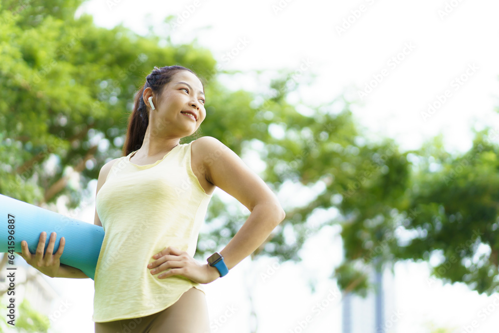 Happy beautiful Asian woman rolling out an exercise - yoga mat on the grass field to prepare doing a yoga and mediation exercise. Woman preparing a yoga or body weight and meditating exercise. Happy beautiful Asian woman rolling out an exercise - yoga mat on the grass field to prepare doing a yoga and mediation exercise. Woman preparing a yoga or body weight and meditating exercise.