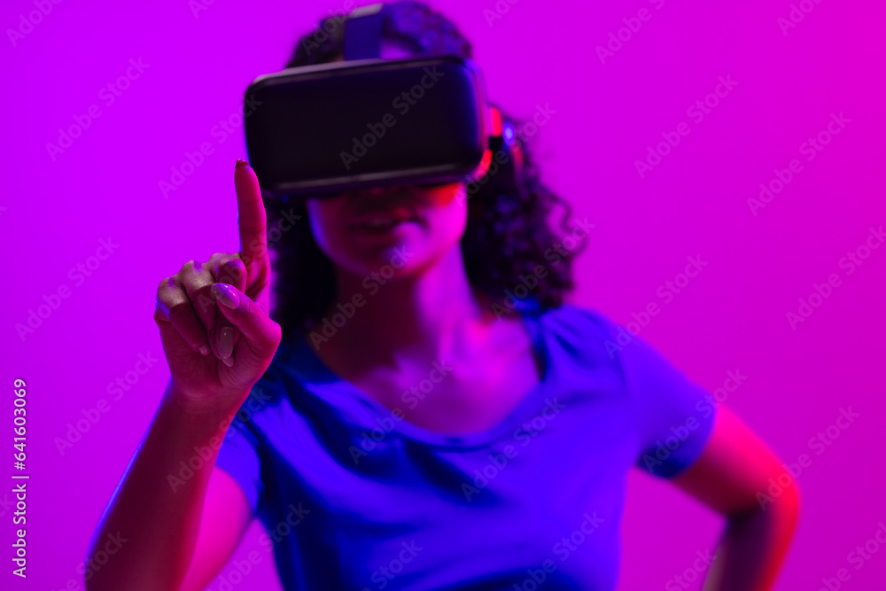 Biracial woman using vr headset and pointing on neon pink to purple background Biracial woman using vr headset and pointing on neon pink to purple background