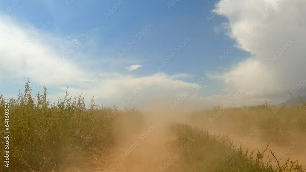 View of the clouds of dust created by a speeding car on a dry country road. Traveling by car in Kyrgyzstan. Blue sky, white clouds and a dusty road. View of the clouds of dust created by a speeding car on a dry country road. Traveling by car in Kyrgyzstan. Blue sky, white clouds and a dusty road.