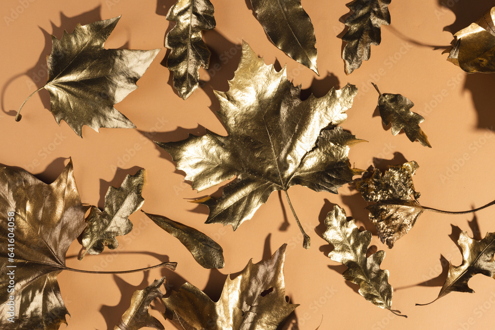 Fototapeta premium Metallic gold autumn leaves lying on orange background