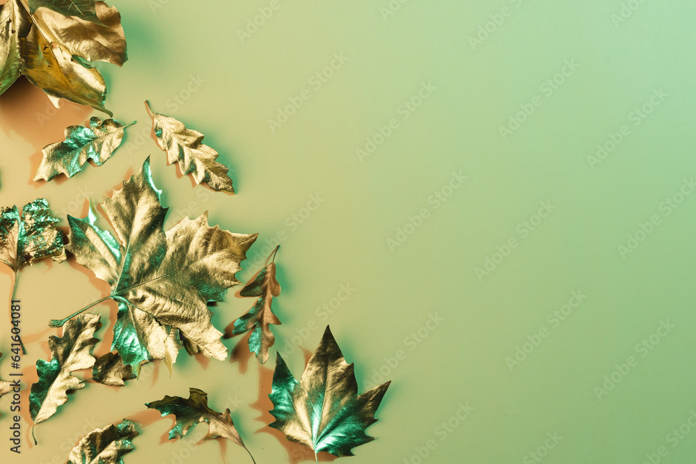 Fototapeta premium Metallic gold autumn leaves with copy space on green background