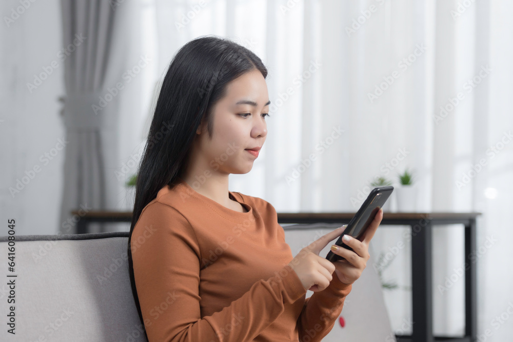 Beautiful Asian woman looking mobile phone laughing with good news or discount voucher for shopping online on a sofa at home. Happy and cheerful woman looking on cellphone app read message feel excite Beautiful Asian woman looking mobile phone laughing with good news or discount voucher for shopping online on a sofa at home. Happy and cheerful woman looking on cellphone app read message feel excite
