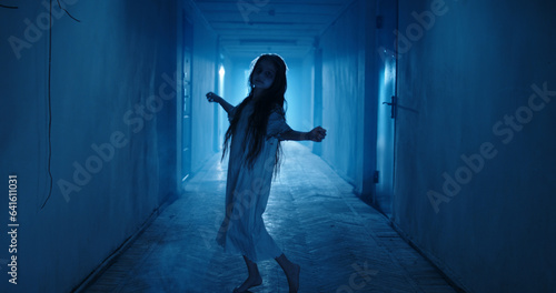Fototapeta Naklejka Na Ścianę i Meble -  Little girl in white dress looking like a ghost carelessly dancing in the hallway of a haunted house - halloween costume party, horror movie 
