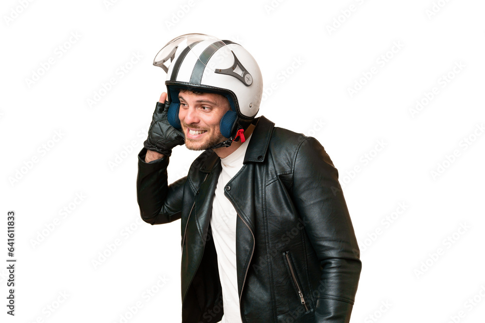Brazilian man with a motorcycle helmet over isolated chroma key background listening to something by putting hand on the ear Brazilian man with a motorcycle helmet over isolated chroma key background listening to something by putting hand on the ear