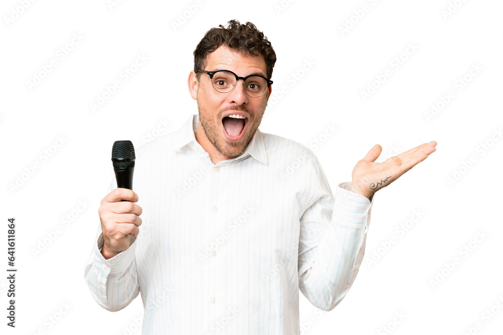 Brazilian man picking up a microphone over isolated chroma key background with shocked facial expression Brazilian man picking up a microphone over isolated chroma key background with shocked facial expression
