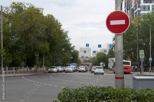 Road sign "no entry" against the background of an intersection with parked cars
