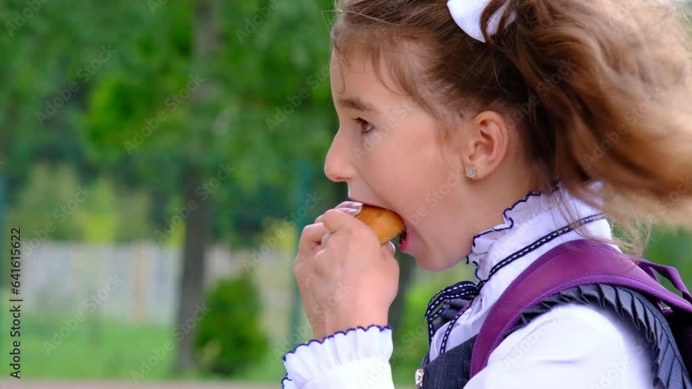 Girl with a backpack eating pie near school. A quick snack with a bun, unhealthy food, lunch from school. Back to school. Education, primary school classes, September 1 Girl with a backpack eating pie near school. A quick snack with a bun, unhealthy food, lunch from school. Back to school. Education, primary school classes, September 1