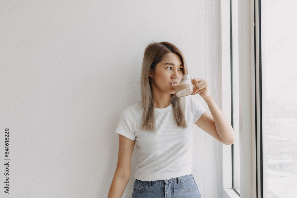 Asian women standing holding drink coffee looking at the window. Asian women standing holding drink coffee looking at the window.