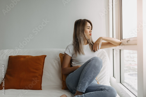 Asian woman sitting on the sofa looking out window at home. Free Download Asian woman sitting on the sofa looking out window at home. - GFXLoad