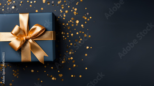 Gift box with golden ribbon and confetti on black background for celebration © wcirco