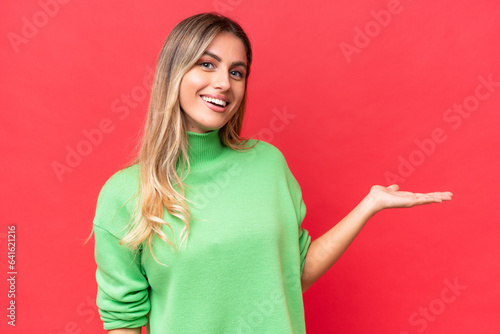 Young Uruguayan woman isolated on red background presenting an idea while looking smiling towards © luismolinero