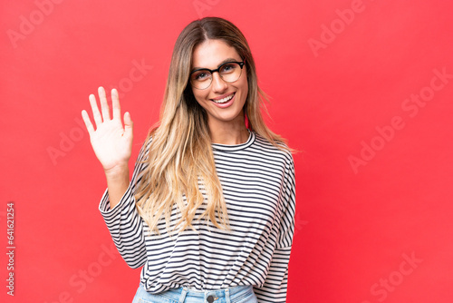 Young Uruguayan woman isolated on red background saluting with hand with happy expression
