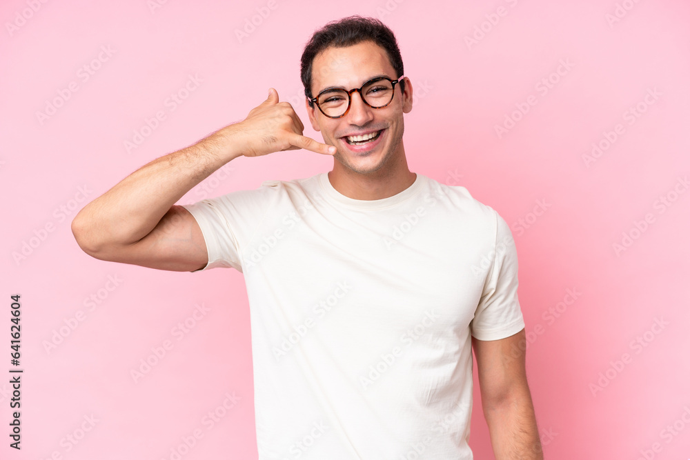 Young caucasian man isolated on pink background making phone gesture. Call me back sign Young caucasian man isolated on pink background making phone gesture. Call me back sign
