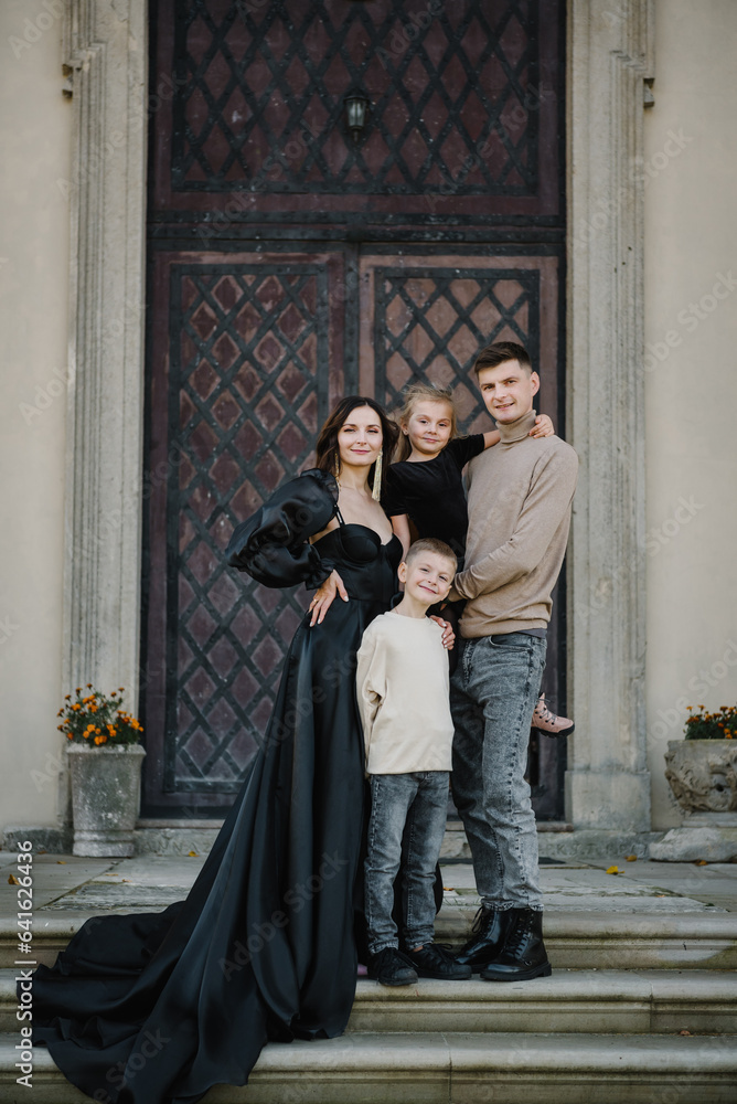 Mother, father, daughter, son stands on steps near large columns of ancient temple at sunset. Parents hugging kids on autumn day. Tourists near Baroque Roman Catholic church in Pidhirtsi, Lviv Ukraine