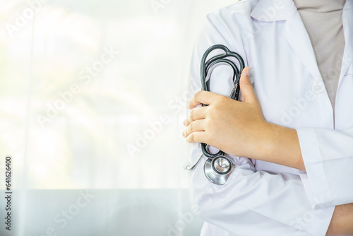 The female doctor held a stethoscope and stood in the ward with a folded arm