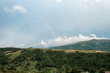 Mountain landscape in cloudy weather and rainbow among clouds