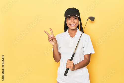 Indonesian female golfer on yellow backdrop showing number two with fingers.