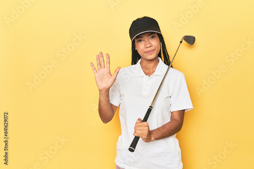Indonesian female golfer on yellow backdrop smiling cheerful showing number five with fingers.