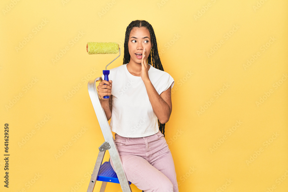 Indonesian woman with roller on ladder on yellow is saying a secret hot braking news and looking aside Indonesian woman with roller on ladder on yellow is saying a secret hot braking news and looking aside
