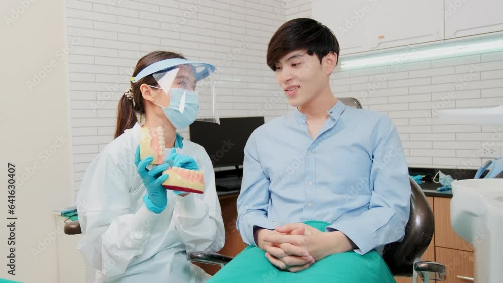 Asian female dentist explaining orthodontic care and whitening to young male patient with teeth model in dental clinic, well-being hygiene, and professional healthcare work in doctor office hospital. Asian female dentist explaining orthodontic care and whitening to young male patient with teeth model in dental clinic, well-being hygiene, and professional healthcare work in doctor office hospital.
