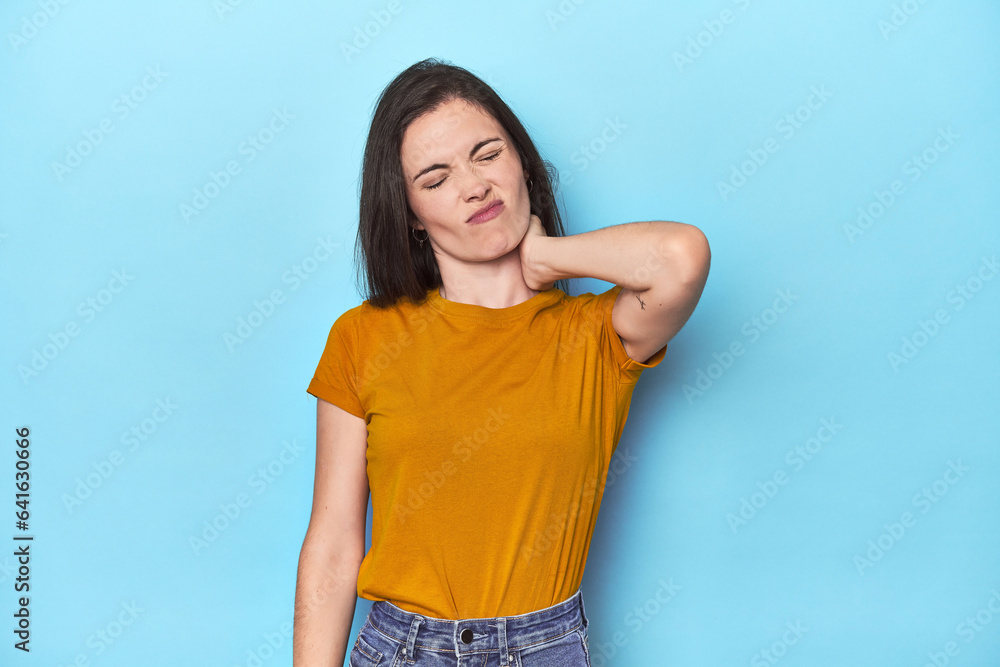 Young caucasian woman on blue backdrop having a neck pain due to stress, massaging and touching it with hand. Young caucasian woman on blue backdrop having a neck pain due to stress, massaging and touching it with hand.