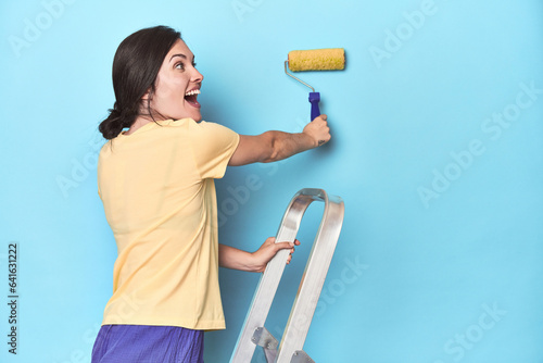 Woman painting a blue wall from a ladder