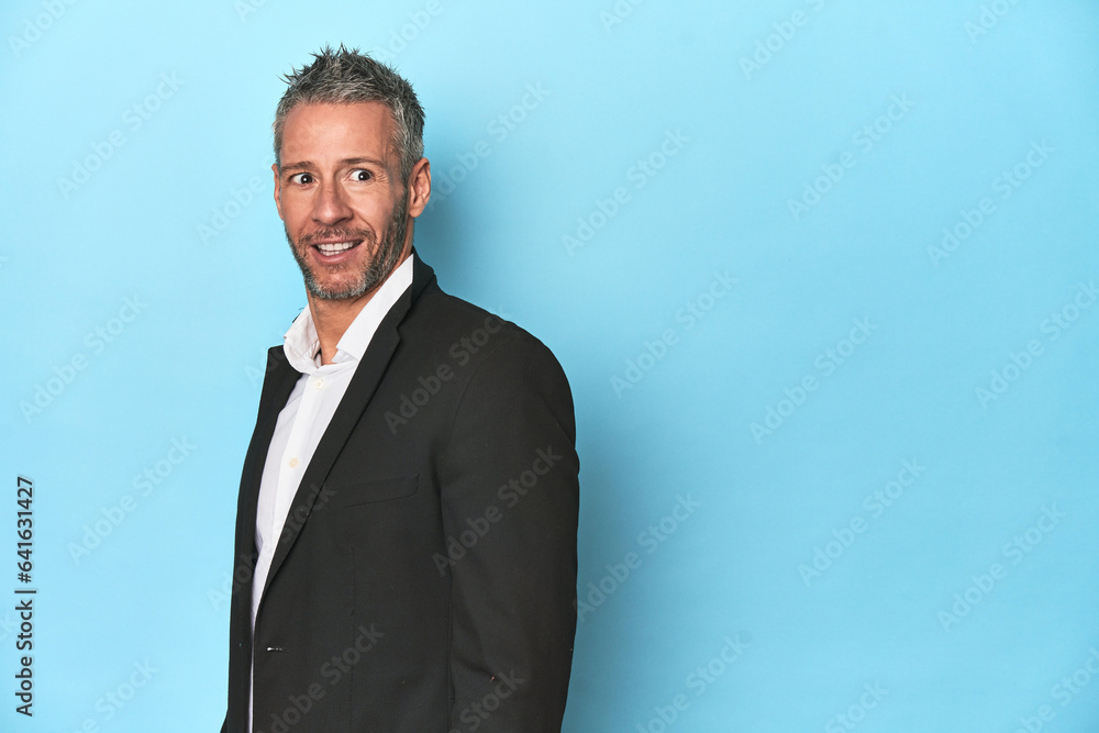 Caucasian businessman, middle-aged on blue background looks aside smiling, cheerful and pleasant. Caucasian businessman, middle-aged on blue background looks aside smiling, cheerful and pleasant.