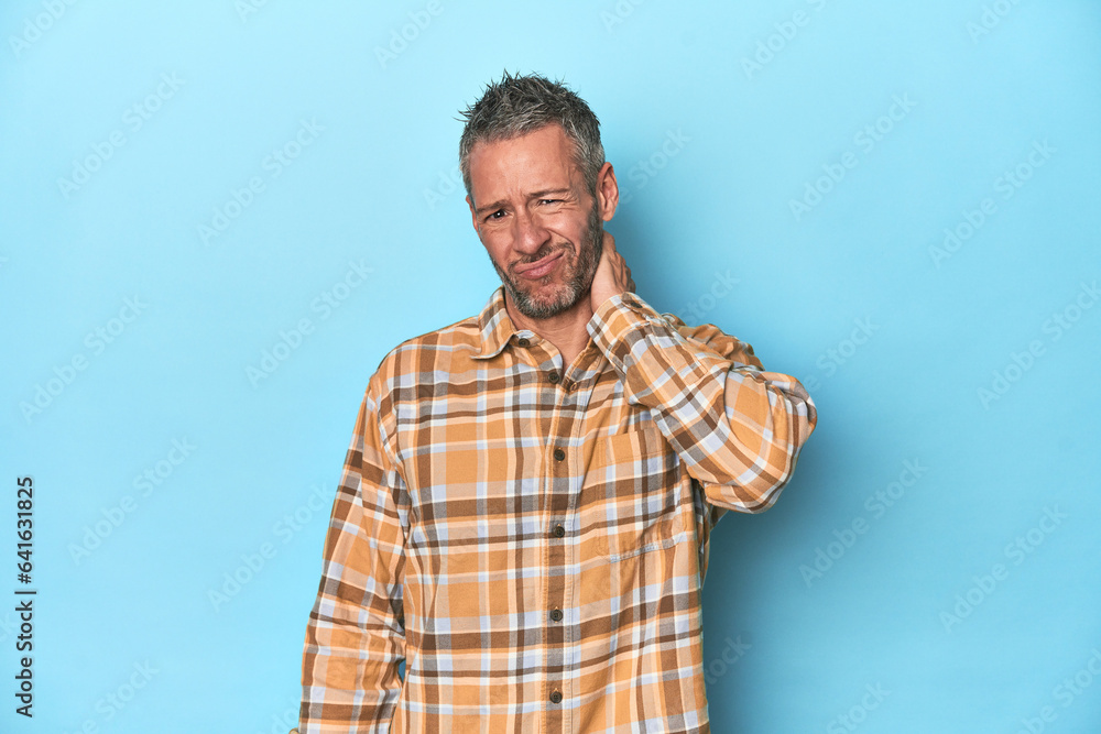 Middle-aged caucasian man on blue backdrop having a neck pain due to stress, massaging and touching it with hand. Middle-aged caucasian man on blue backdrop having a neck pain due to stress, massaging and touching it with hand.