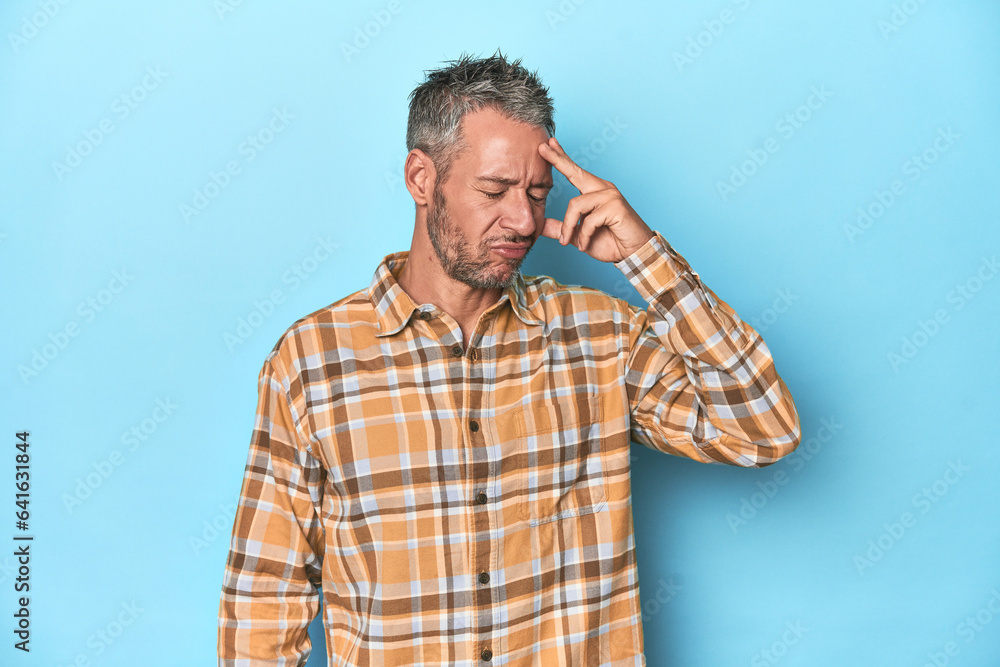 Middle-aged caucasian man on blue backdrop having a head ache, touching front of the face. Middle-aged caucasian man on blue backdrop having a head ache, touching front of the face.