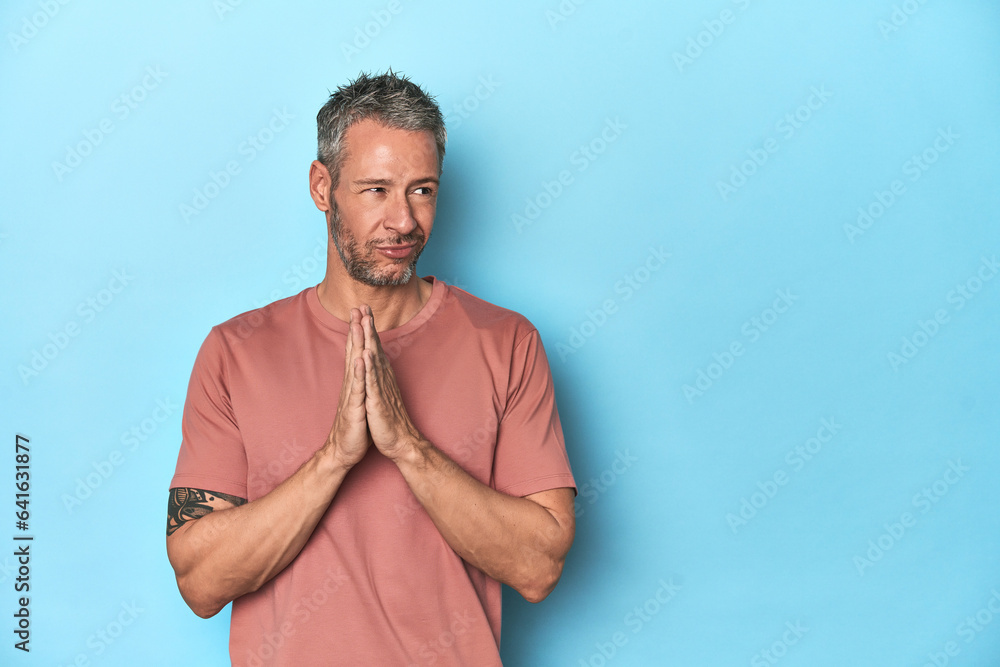 Middle-aged caucasian man on blue backdrop making up plan in mind, setting up an idea. Middle-aged caucasian man on blue backdrop making up plan in mind, setting up an idea.