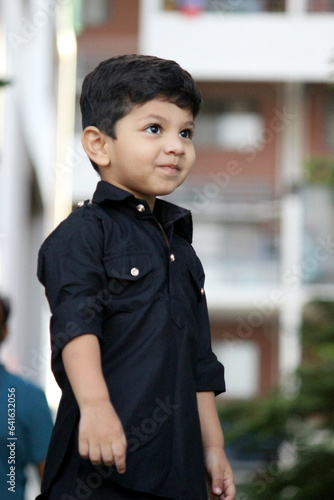 Cute and curious boy standing and looking at someone, He is wearing black pathani kurta and in a festive mood. adorable child with naughty expression standing outdoor. handsome black pathani outfit. photo