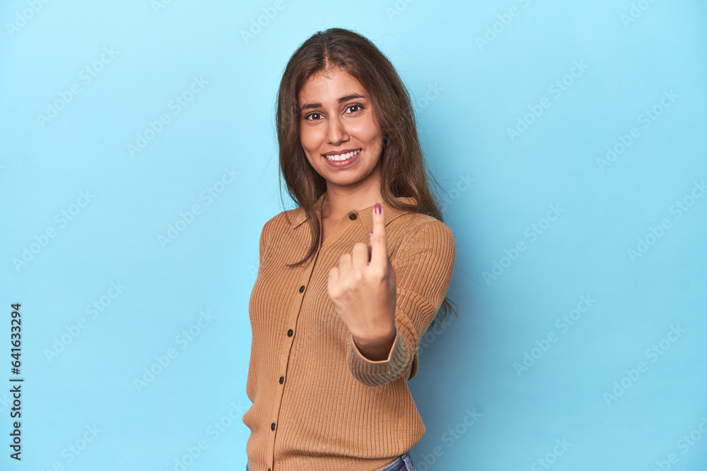 Teen girl in brown polo shirt on blue pointing with finger at you as if inviting come closer. Teen girl in brown polo shirt on blue pointing with finger at you as if inviting come closer.