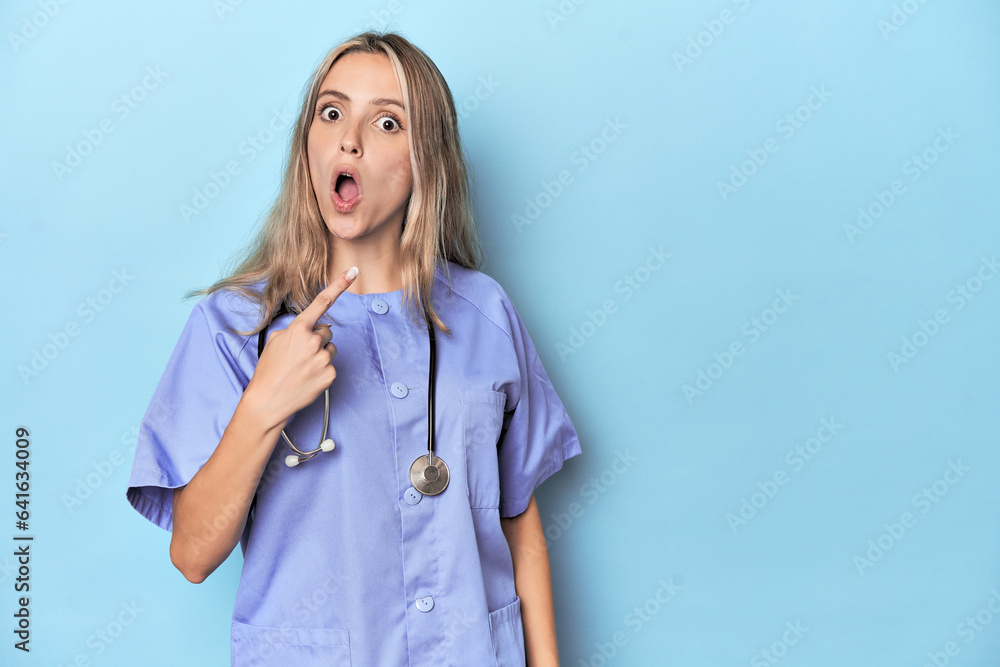 Young caucasian nurse in blue studio pointing to the side Young caucasian nurse in blue studio pointing to the side