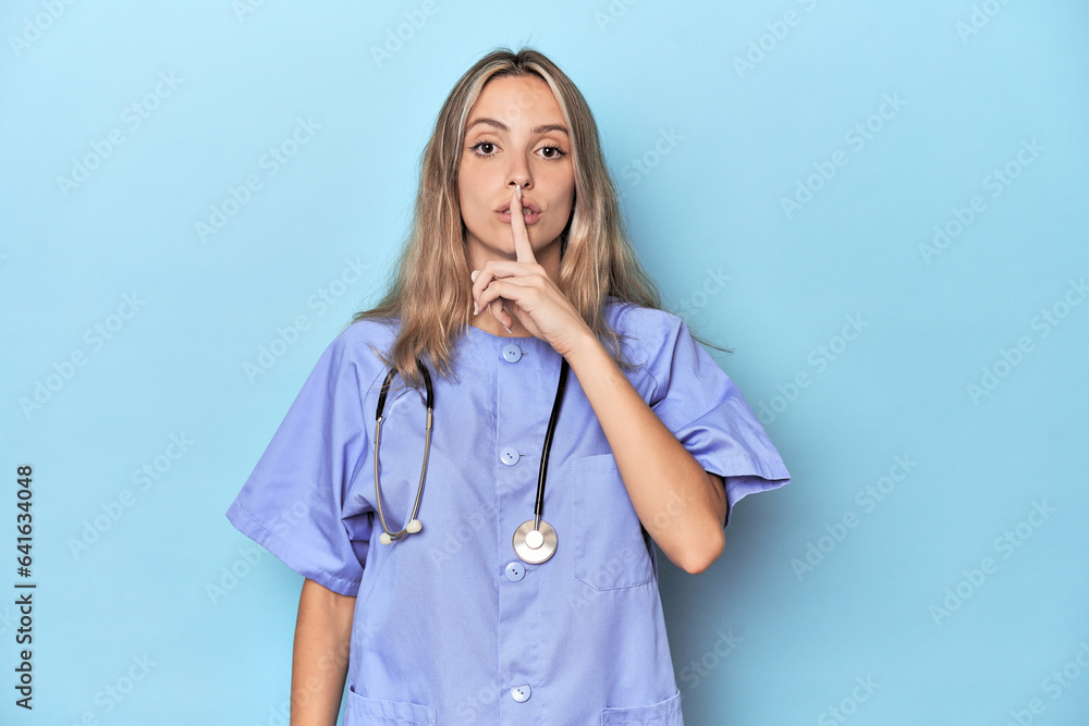 Young caucasian nurse in blue studio keeping a secret or asking for silence. Young caucasian nurse in blue studio keeping a secret or asking for silence.