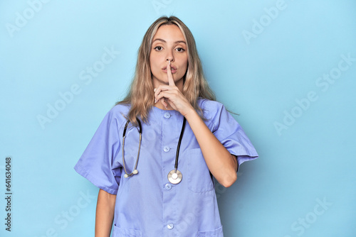 Young caucasian nurse in blue studio keeping a secret or asking for silence.