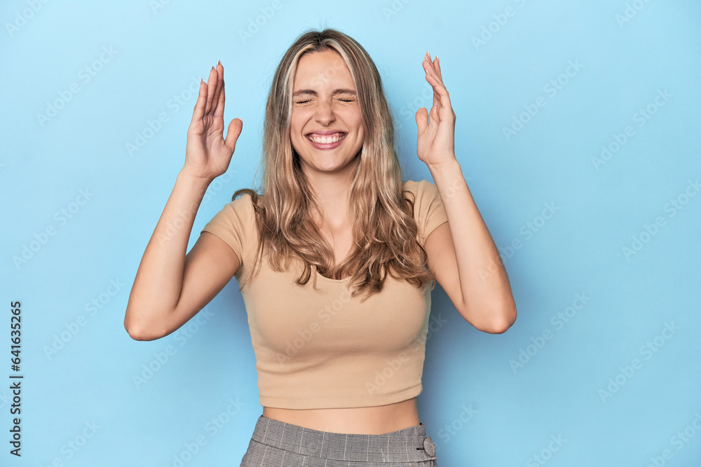 Blonde young caucasian woman in blue studio joyful laughing a lot. Happiness concept.