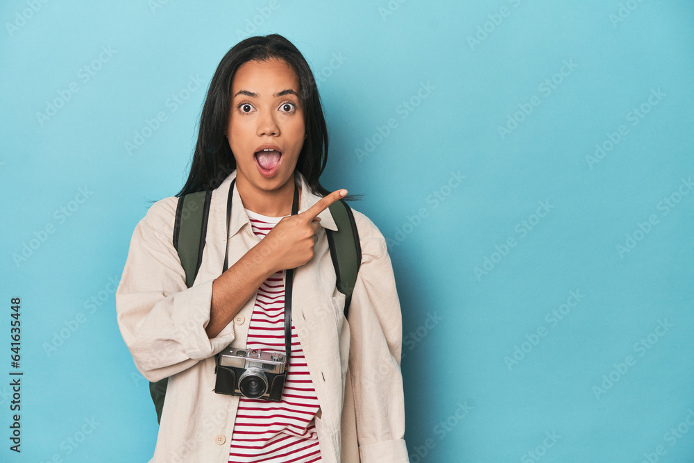 Filipina woman with camera and backpack on bluepointing to the side Filipina woman with camera and backpack on bluepointing to the side