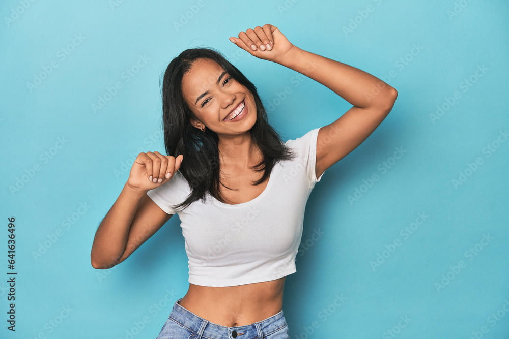 Filipina young woman on blue studio celebrating a special day, jumps and raise arms with energy. Filipina young woman on blue studio celebrating a special day, jumps and raise arms with energy.