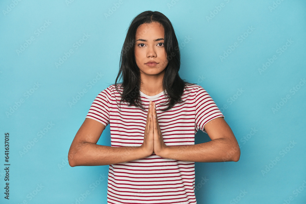 Filipina young woman on blue studio praying, showing devotion, religious person looking for divine inspiration. Filipina young woman on blue studio praying, showing devotion, religious person looking for divine inspiration.