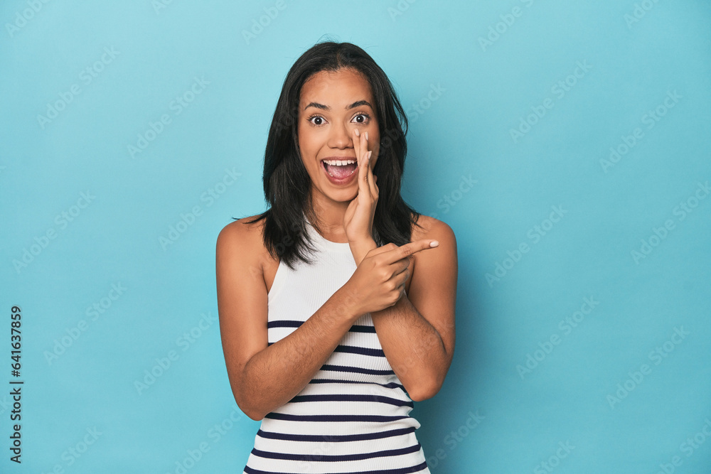 Filipina young woman on blue studio saying a gossip, pointing to side reporting something. Filipina young woman on blue studio saying a gossip, pointing to side reporting something.